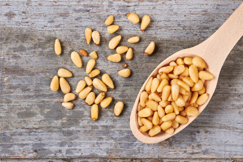 A spoonful of pine nuts with some scattered on a table