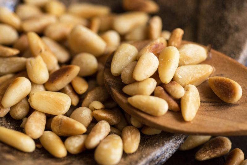 Pine nuts on some type of board with some being lifted out and placed on a spoon