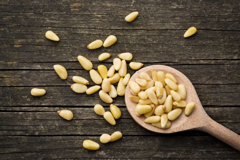 A dark wooden background with pine nuts, some of which are on a wooden spoon