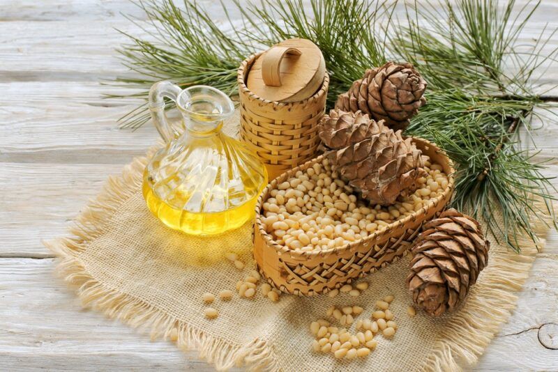 Three pine cones on top of a dish of pine nuts, next to pine branches and oil