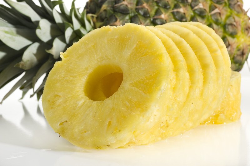 This photo shows a row of pineapple slices in front of a whole pineapple on a white background.