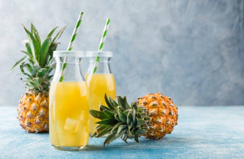 Two bottles of pineapple juice with two fresh pineapples on a table