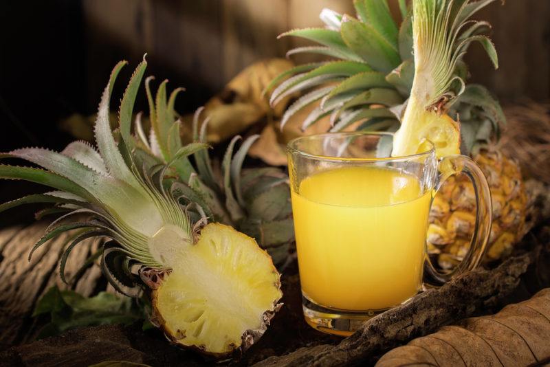 A glass of pineapple juice with various pineapples