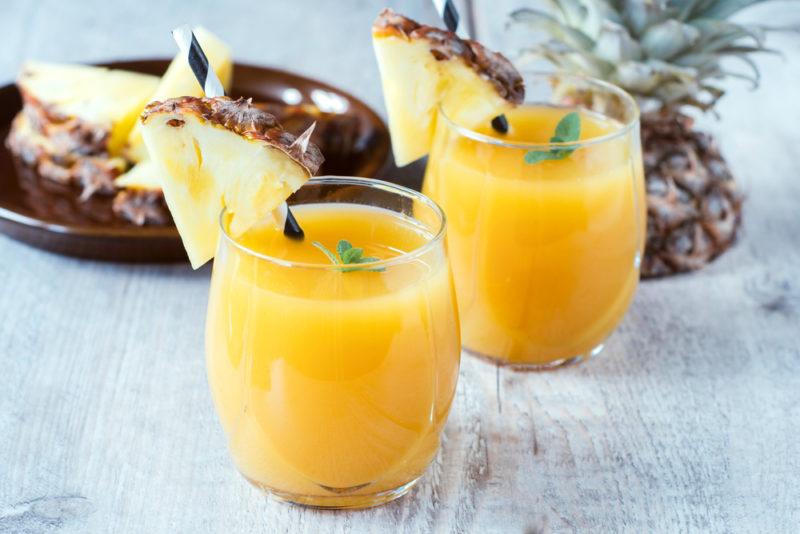 Two glasses of pineapple juice, with pineapple wedges and pineapple in the background