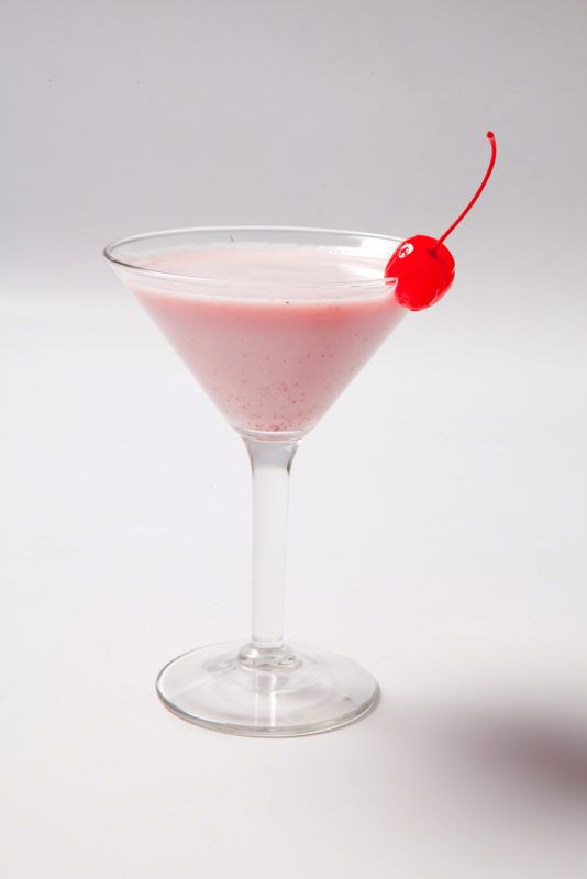 A cocktail glass with a creamy pink lady drink and a glace cherry