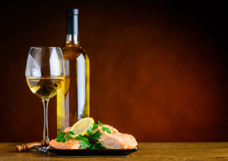 A bottle of pinot gris next to a glass of the wine and some salmon