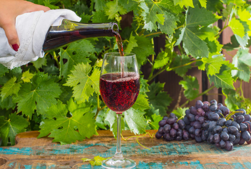 A glass of pinot noir wine being poured from a bottle next to some grapes