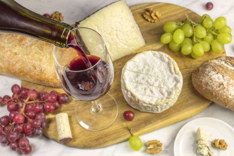 A cheese board with wine, various types of cheeses, grapes, and nuts