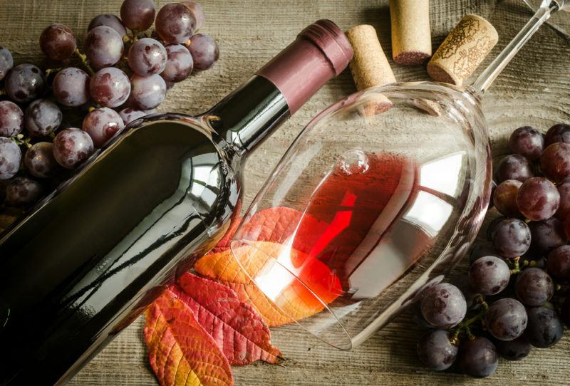 A bottle of pinot noir, a glass with a little wine in it, an autumn leaf, two bunches of grapes and some wine corks