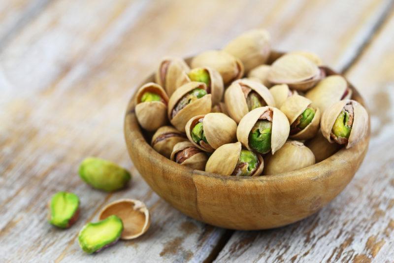 A wooden bowl containing pistachio nuts