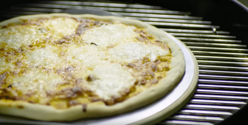 pizza on pizza stone and the pizza stone is on a charcoal grill grate