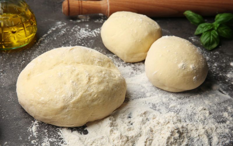 Three balls on pizza dough on a table with flour