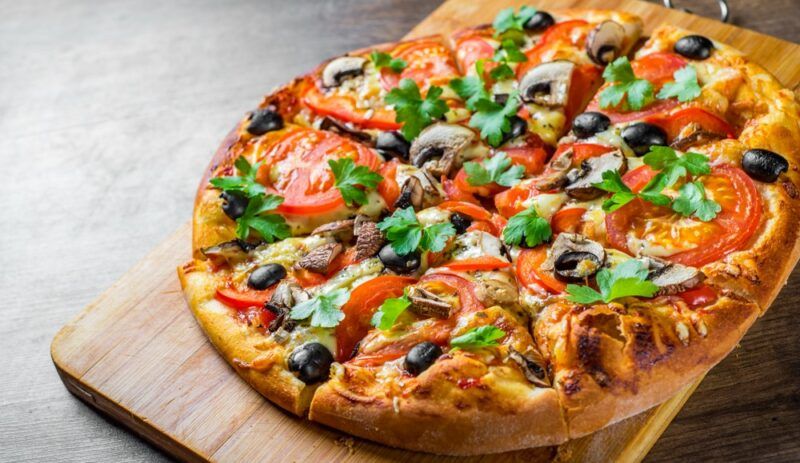 A fresh pizza with a variety of toppings, including mushrooms, tomatoes, spinach, and olives