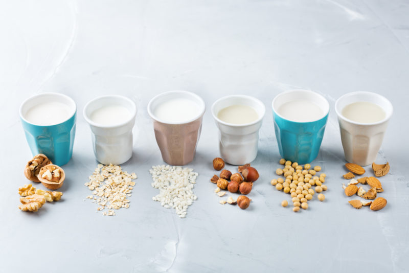 Mugs of plant-based milk with the milk source in front of each mug