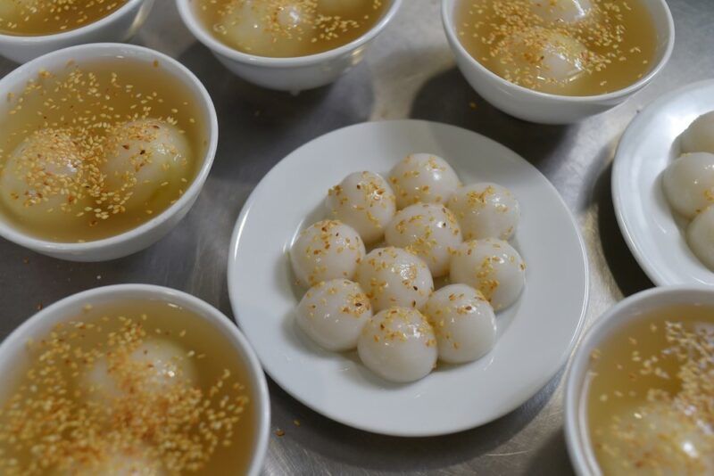 A white plate containing banh troi balls, with bowls of banh troi in broth surrounding the plate