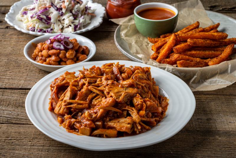 A plate of pulled pork alternative made from shredded jackfruit, with more bbq like foods in the background