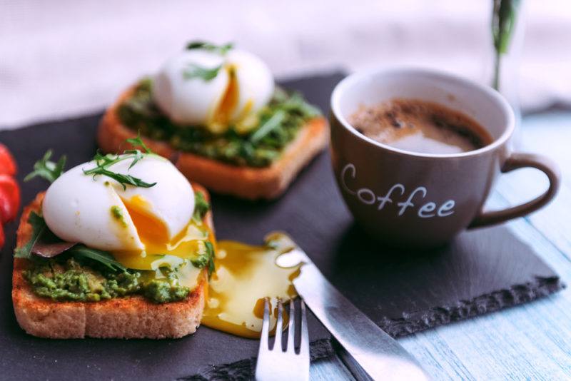 Two poached eggs on toast with pesto, next to a knife and fork and a coffee cup.