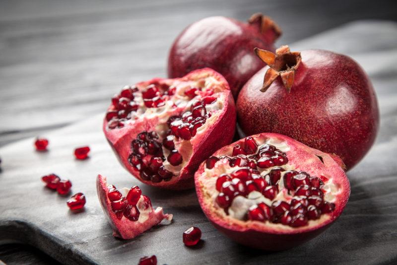 Two pomegrantes on a table with another sliced pomegranate on a table