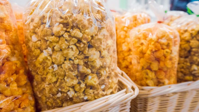 Several varieties of popcorn in clear plastic bags rest in wicker baskets.