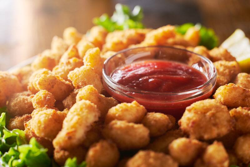 Piles of popcorn shrimp surround a clear glass bowl filled with cocktail sauce.