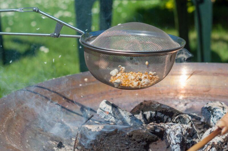 Someone holding a mesh basket over a fire to make popcorn