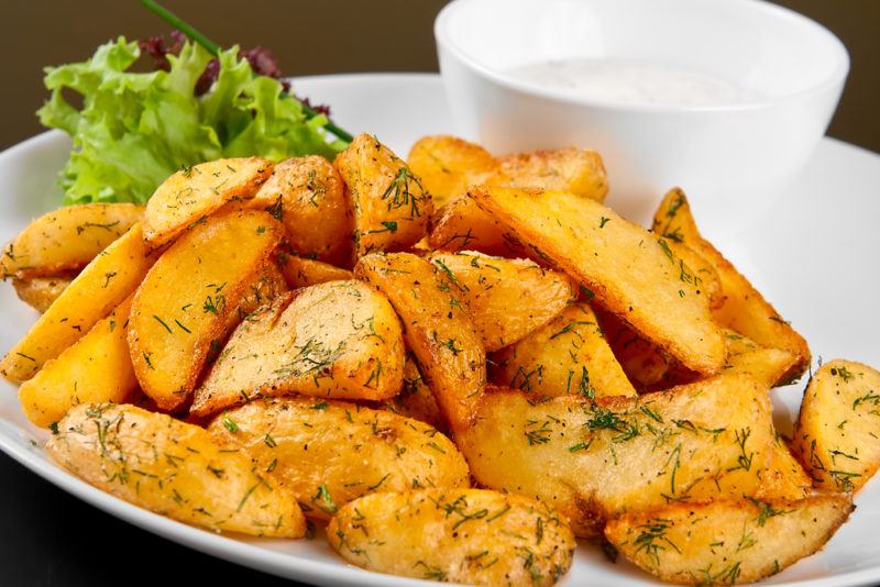 A white dish with cooked potato wedges