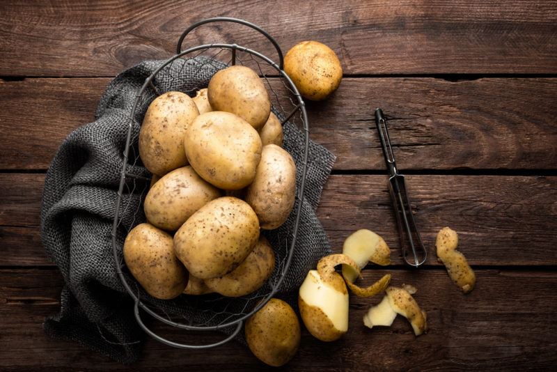 A basket of potatoes, some of which have been peeled