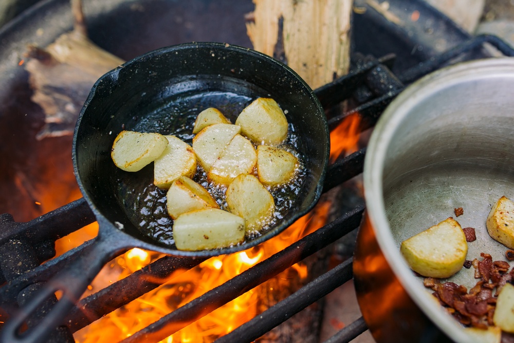 A frypan with potatoes over a campfire