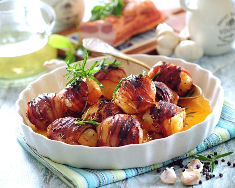 A white dish of potatoes that have been wrapped in bacon