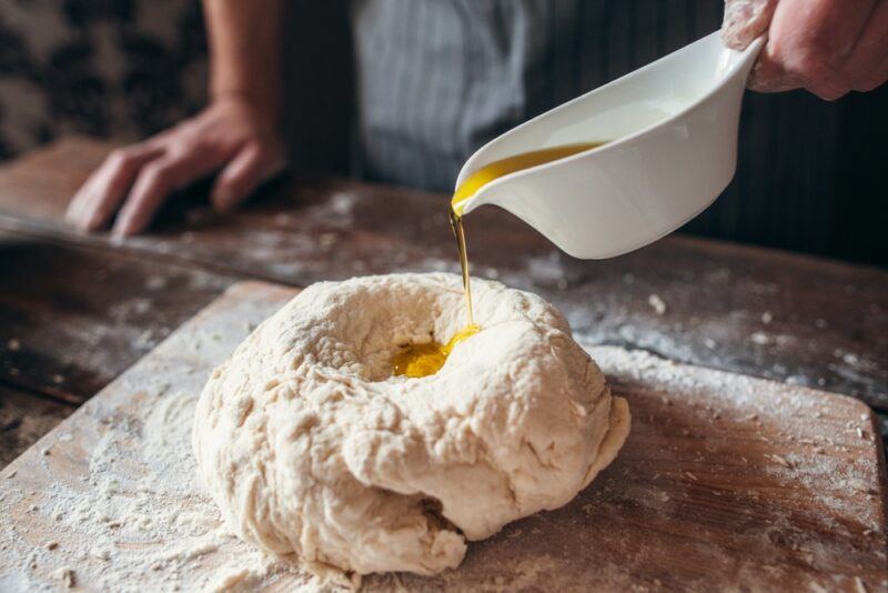 Someone making pizza dough or bread, pouring olive oil into a well in the center of their dough