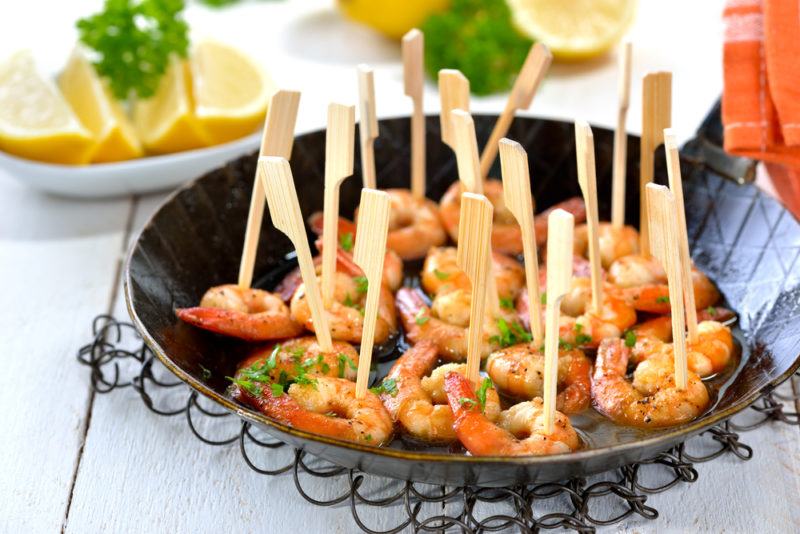 A black fry pan that contains prawns with cocktail sticks