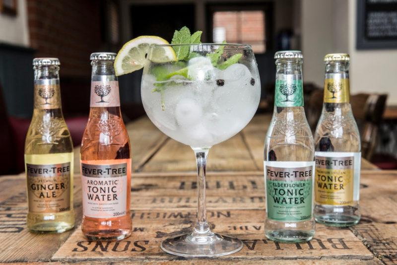 Four bottles of Fever Tree tonic water surrrounding a large glass of gin and tonic