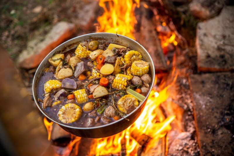 A pot over a campfire, being used to prepare a stew