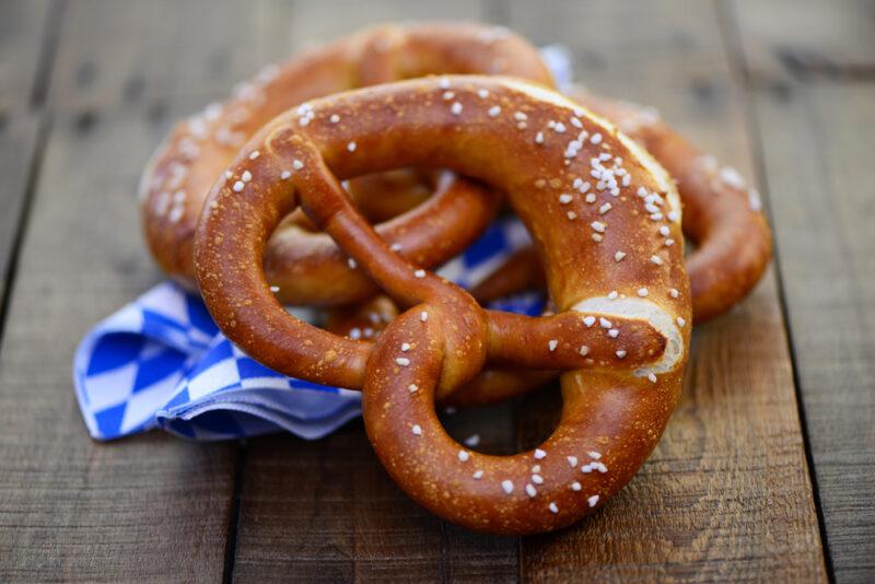 Three large pretzels rest on a blue and white napkin on a wooden table.