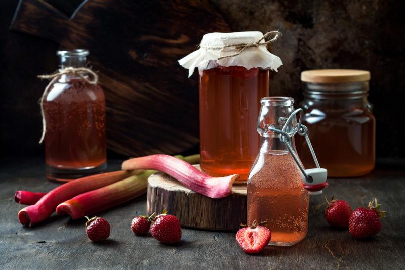 Various bottles and jars with probiotic lemonade, with rhubarb and strawberries on the table