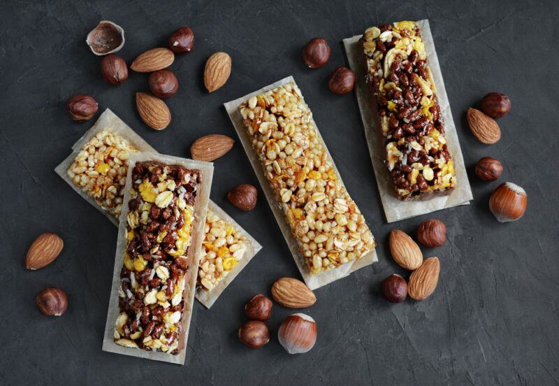 A selection of protein bars made with nuts, and various nuts scattered on the table