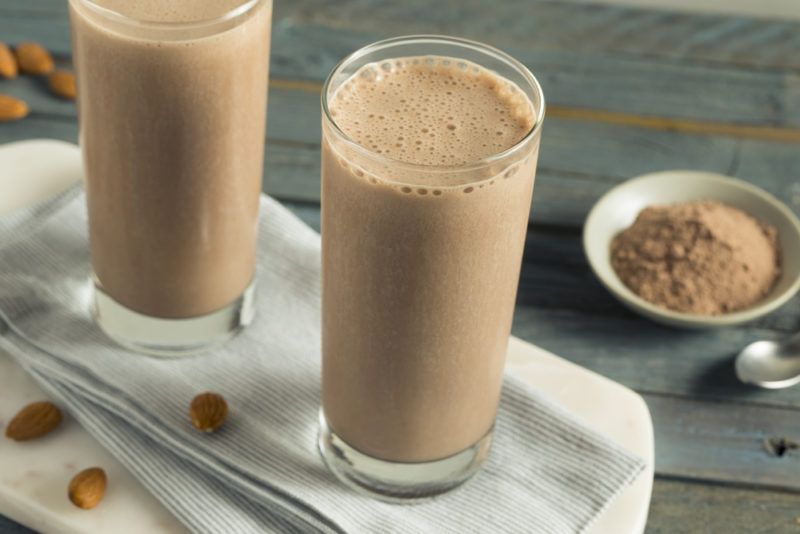 Two glasses containing chocolate protein shake next to some almonds