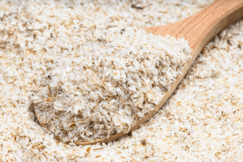 A large pile of psyllium husk power, with a wooden spoon lifting some powder away from the rest.