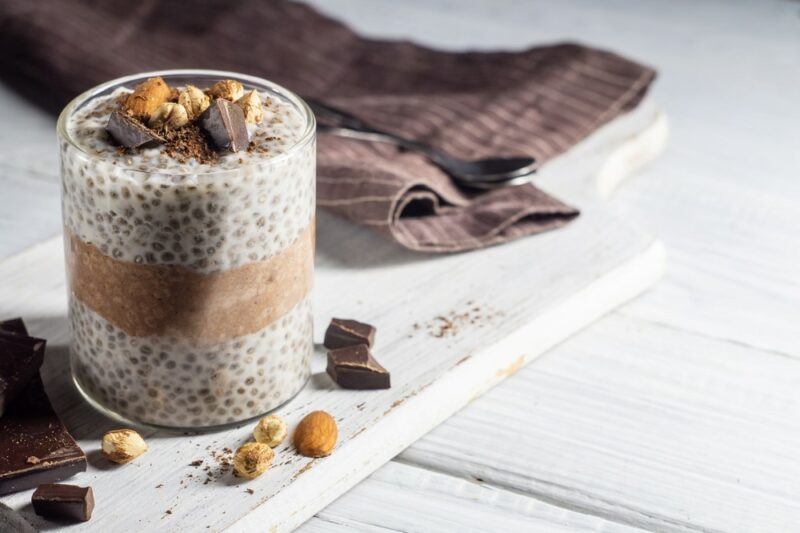 A glass filled with a pudding made from chia seeds and pumpkin on a white plate and a white table