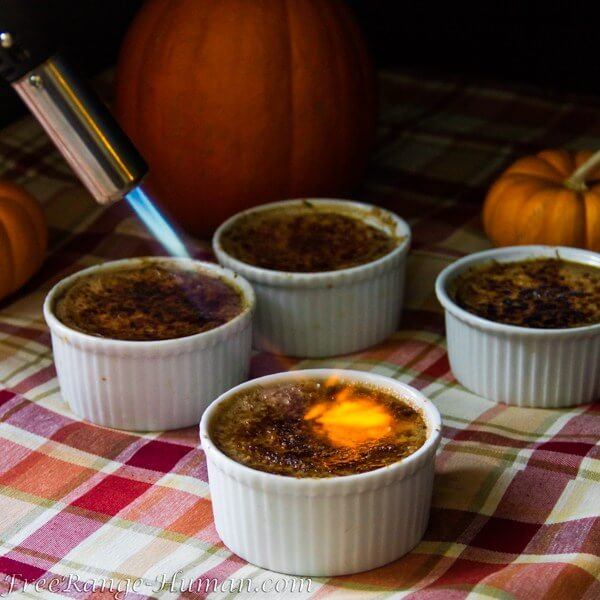 Four white pots containing creme brulee. One of them is being finished using a blow torch. 