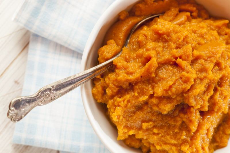 A white bowl with a spoon that contains pumpkin puree