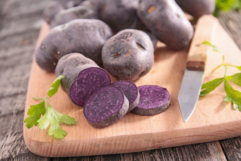 Purple potatoes on a cutting board with one of them being cut open. 