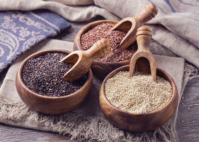 Three wooden bowls containing quinoa and spoons