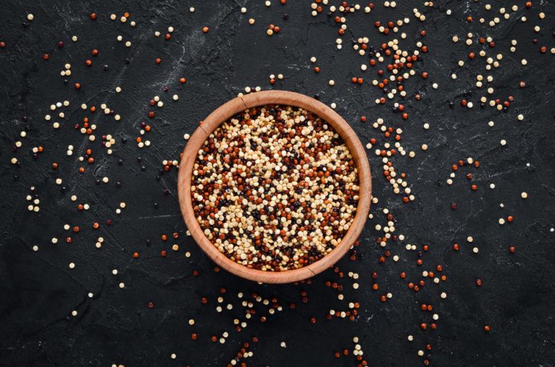 A wooden bowl containing quinoa on a black background