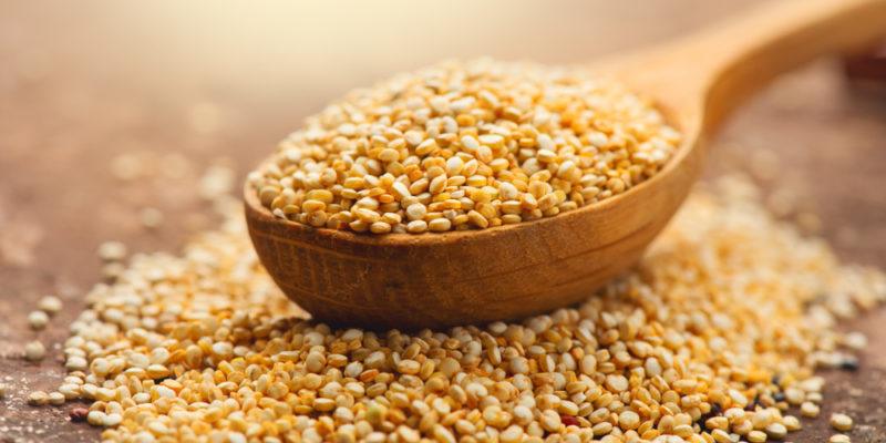 A wooden spoon containing quinoa on a wooden table