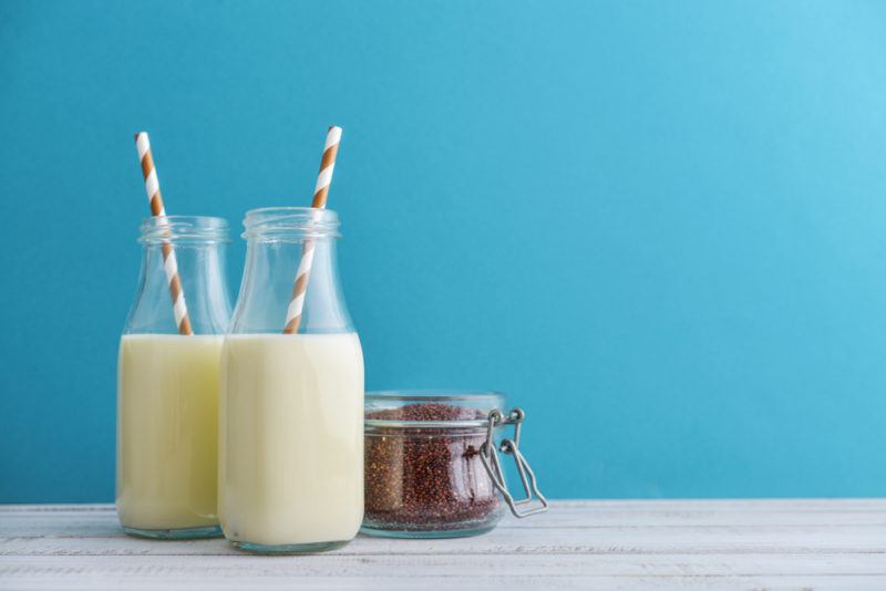 Two bottles of quinoa milk with straws, next to a glass container of quinoa