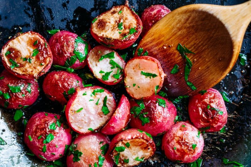 Radish halves that have been cooked, with a wooden spoon