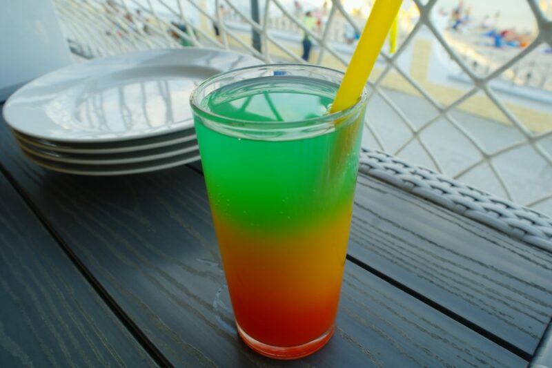 A glass on a table in front of a stack of plates. It contains loaded tea that's been layered to form a traffic light design.