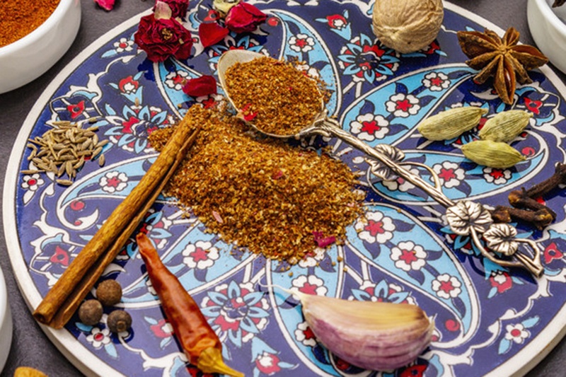 closeup image of a blue decorative plate with different spices and a mound of ras el hanout at the middle