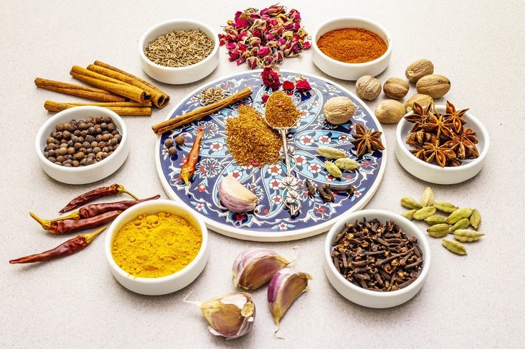 different bowls containing different spices for Ras el hanout with whole spices in between the bowls, at the middle is a printed plate with other whole spices with Ras el hanout powder at the middle